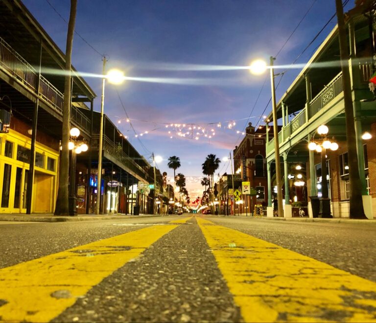 7th Avenue in Ybor City at dusk, string lights overhead, palm trees, and historic buildings with wrought-iron balconies
