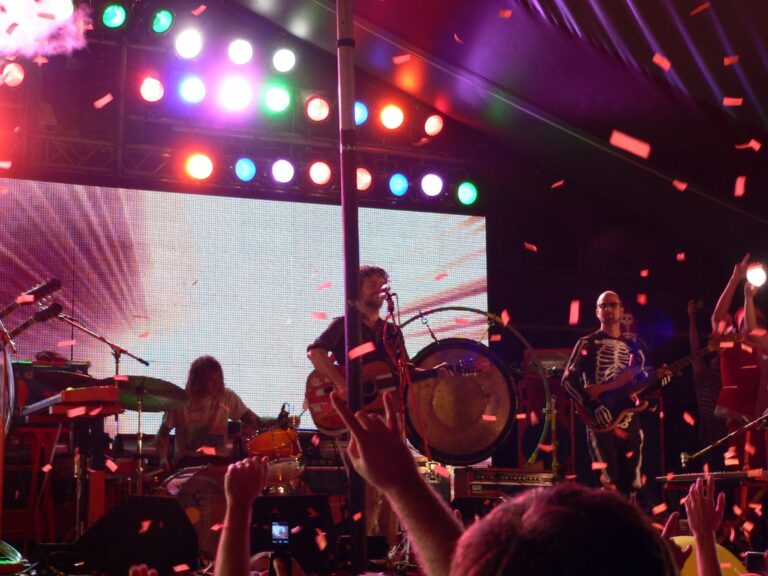 Band performing on a brightly lit outdoor stage as confetti falls over the crowd