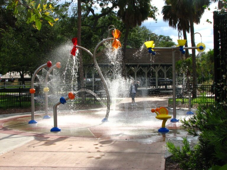 Children's splash pad at Ballast Point Park in Tampa, with colorful water-play equipment spraying water into the air above a wet concrete pad.