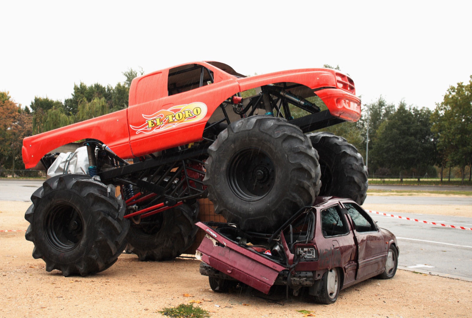 A monster truck driving over a crushed car